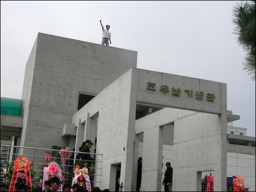 시민단체 한 회원이 건물 옥상에 올라가 밀가루를 던지며 "황철곤 시장은 사퇴하라"고 외치고 있다. 